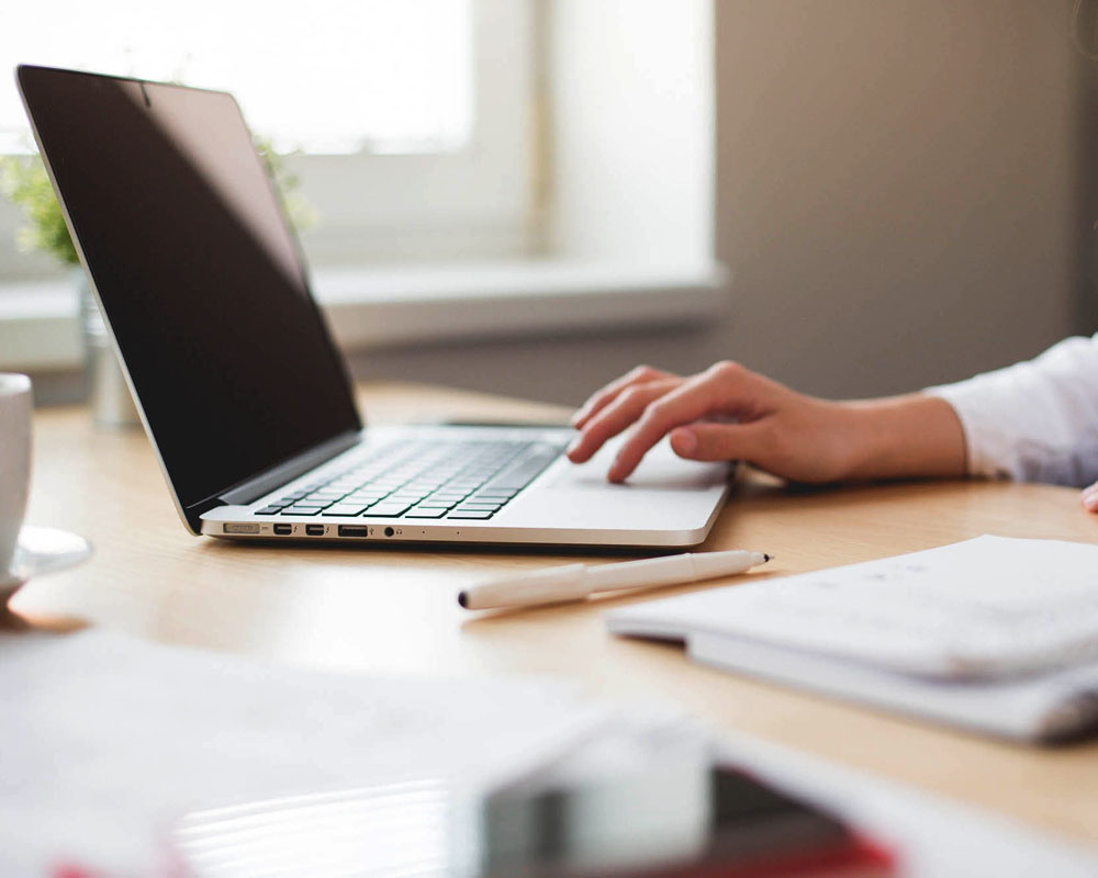 dettaglio di mani che lavorano al computer. Scrivania con quaderno e penna