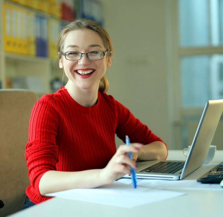 ragazza sorridente alla scrivania con computer portatile e penna in mano